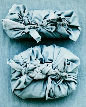 Two fabric-wrapped packages tied and knotted with cloth strips resting against a textured blue background.