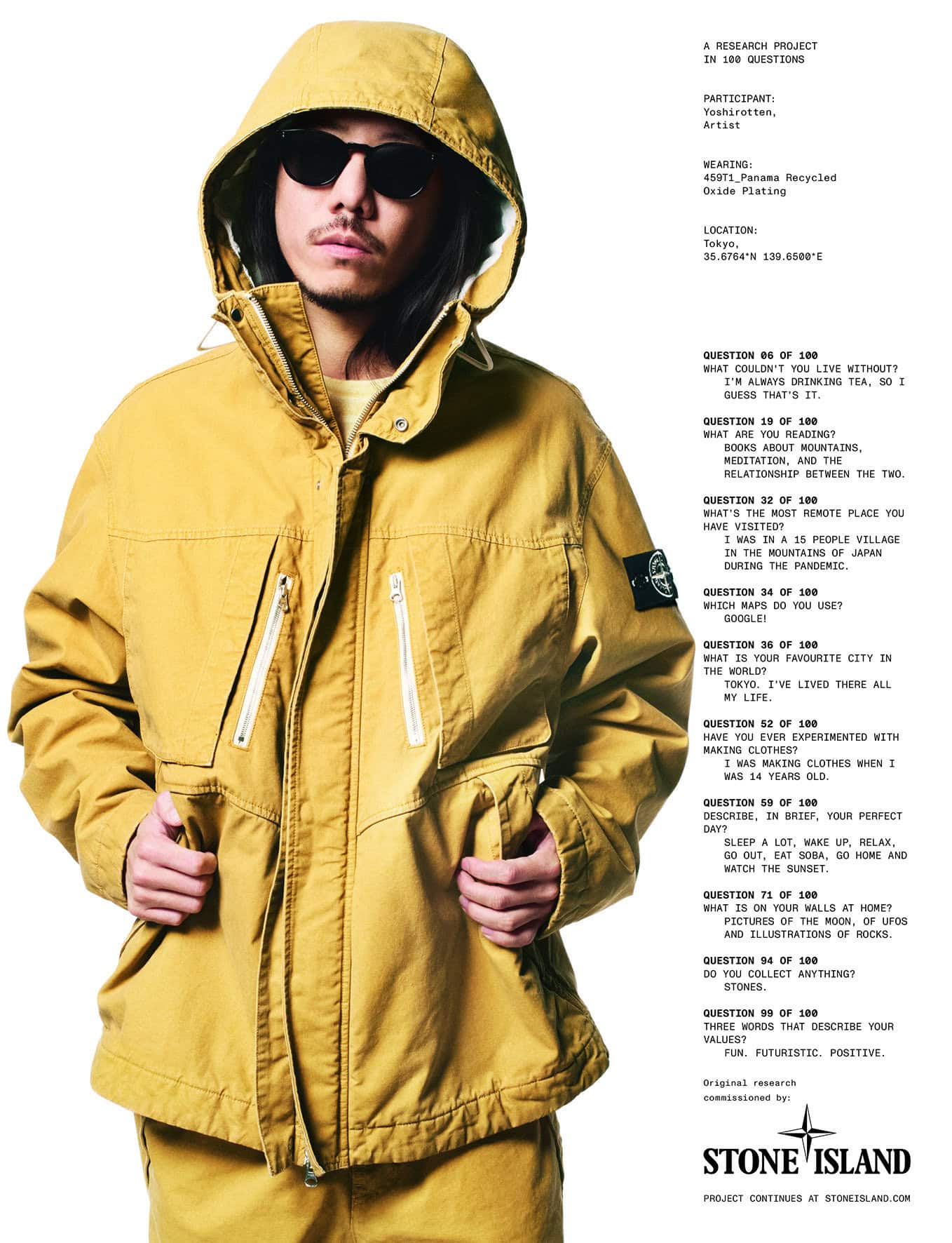 Man with sunglasses posing in a mustard-yellow hooded jacket and matching pants against a white backdrop with Stone Island text.