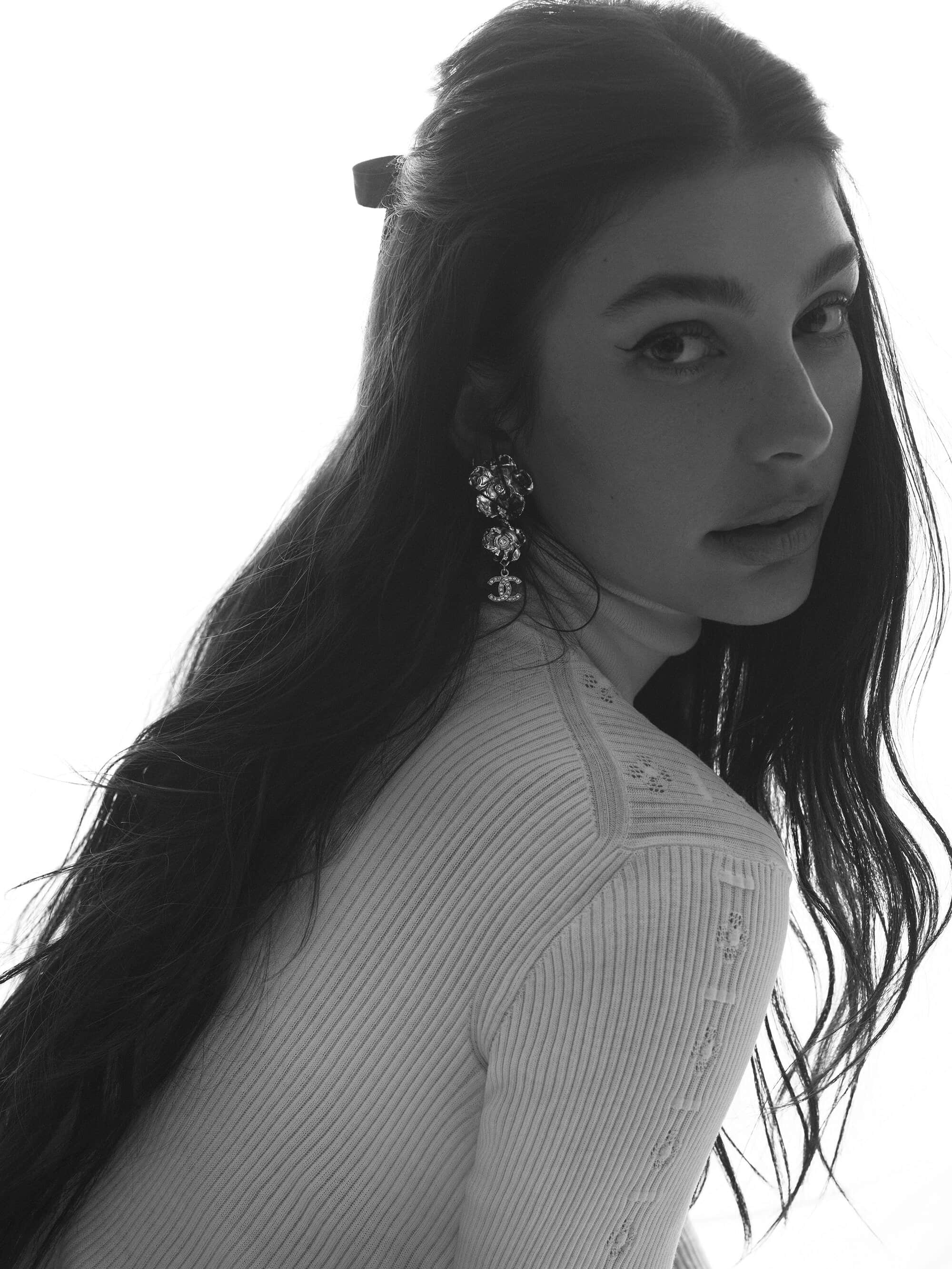 Black and white portrait of a brunette woman wearing drop earrings and a light colored turtle neck sweater against a white background.