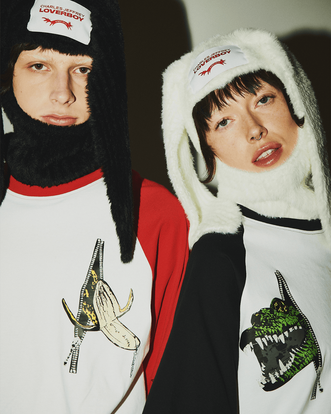 Two people wearing Charles Jeffrey Loverboy bunny hats and graphic T-shirts in a studio setting; fashion forward, bright lighting.