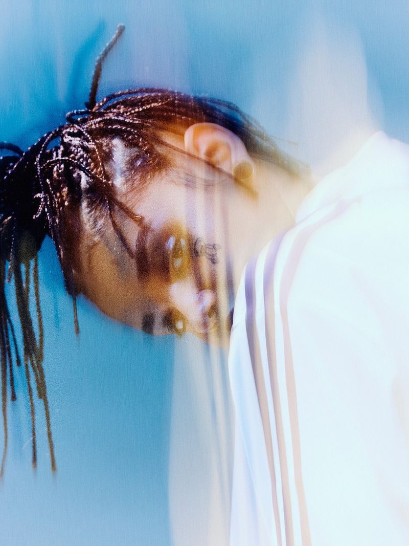 Portrait of a young Black woman with braids in a white hooded sweatshirt against a blurred blue background in a studio setting.