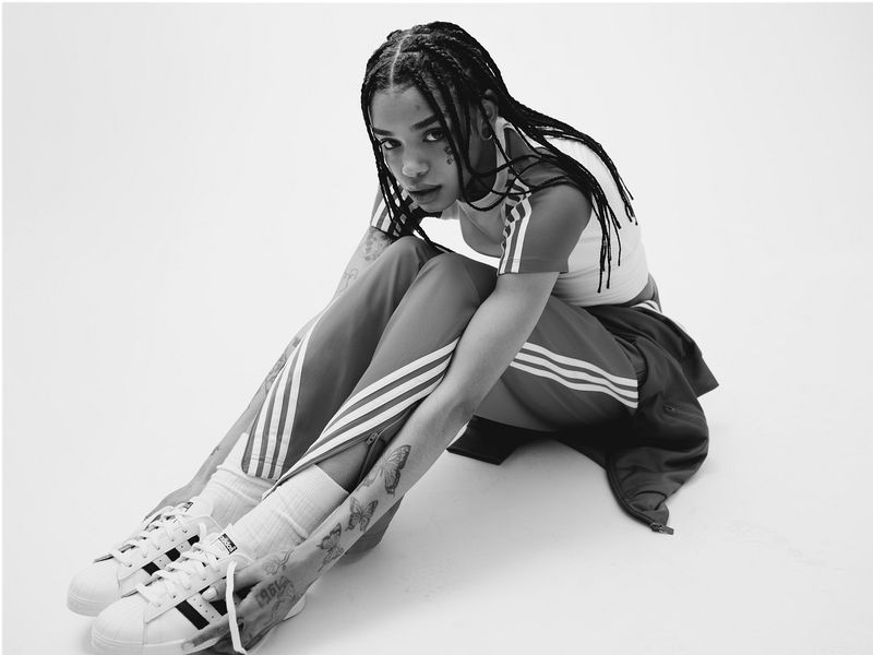Black and white image of a woman in athletic wear sitting with her legs out in front of her, Adidas sneakers are visible.