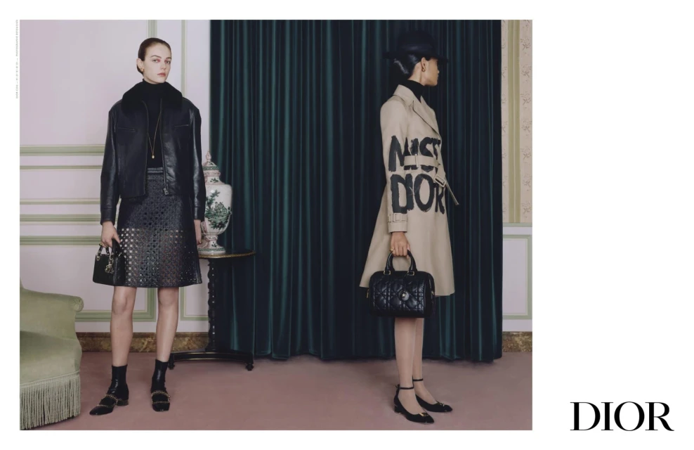 Two fashion models pose indoors wearing Dior jackets and skirts, holding Dior bags, with a green curtain background.