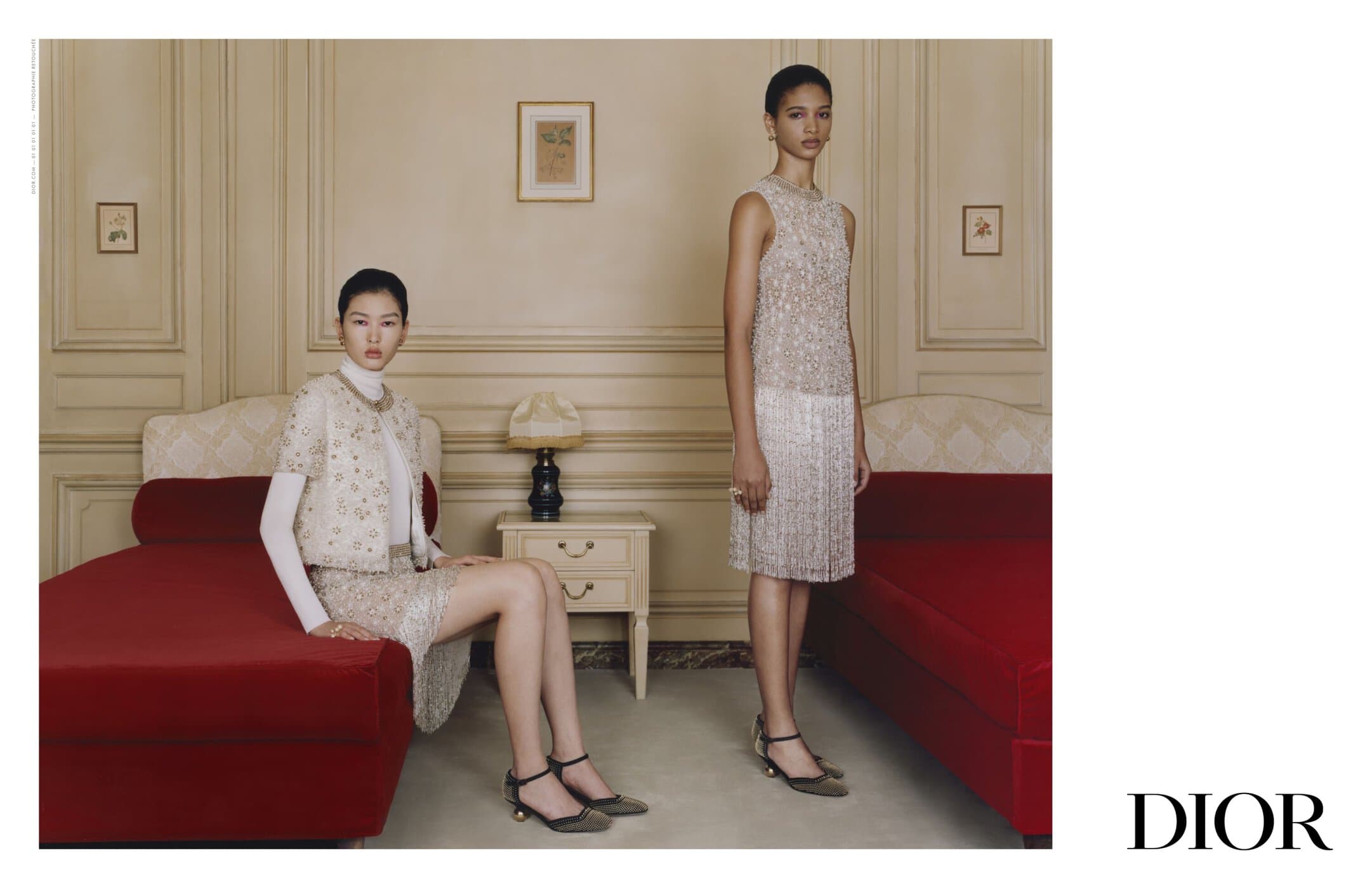 Two women in elegant, beaded dresses pose in an indoor setting with red couches, showcasing a blend of fashion and interior design.