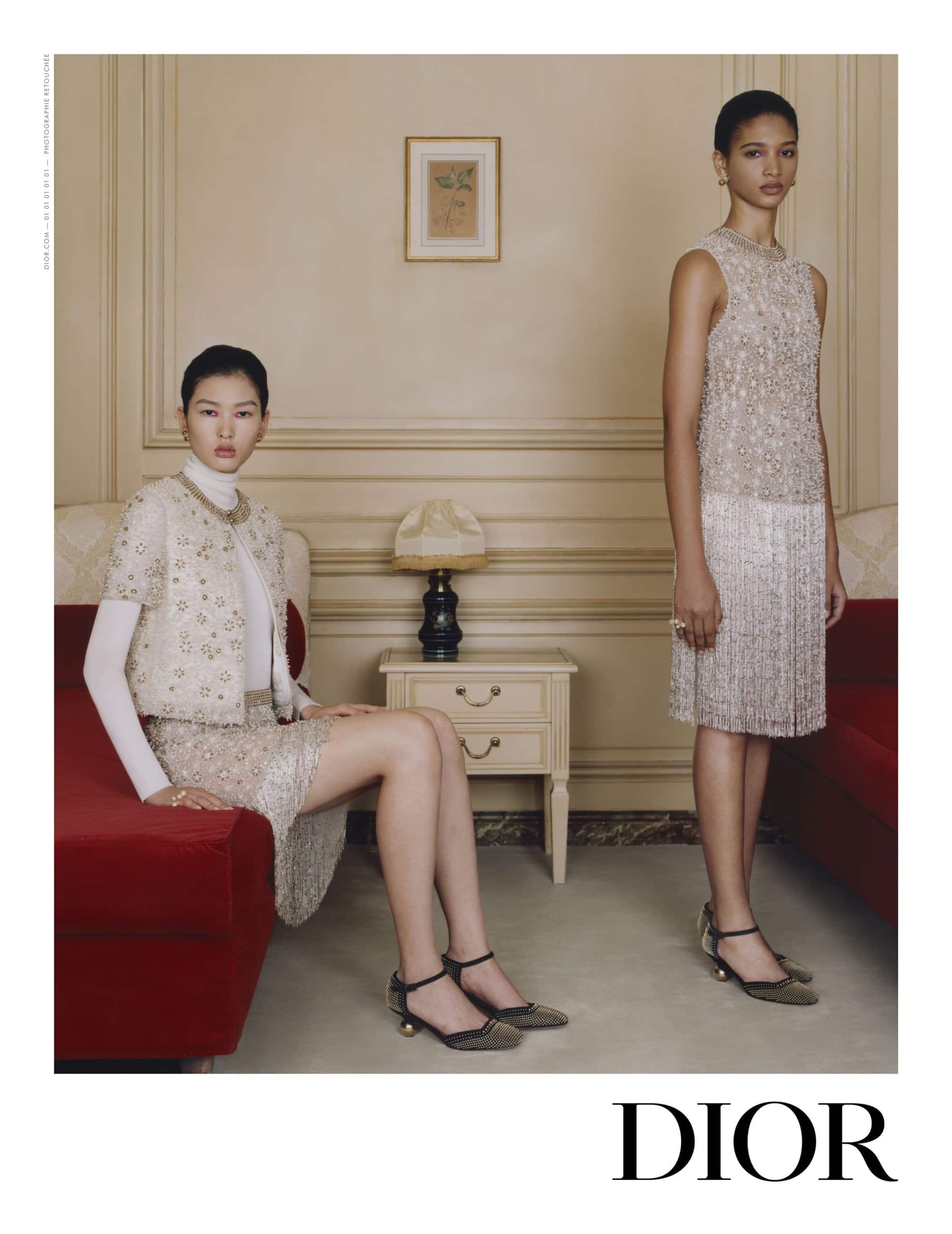 Two elegant Asian women showcase couture fashion indoors. They are wearing ornate embellished skirt suits by Dior, posing in front of a wall.
