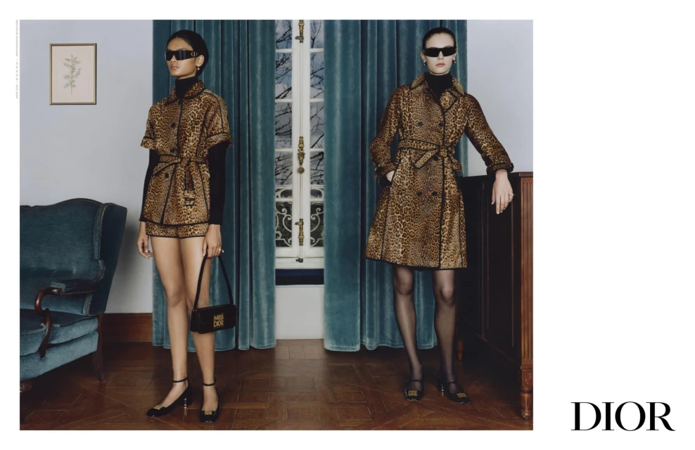 Two women showcase elegant leopard-print outfits with a modern touch, paired with stylish accessories, set against a softly lit interior.