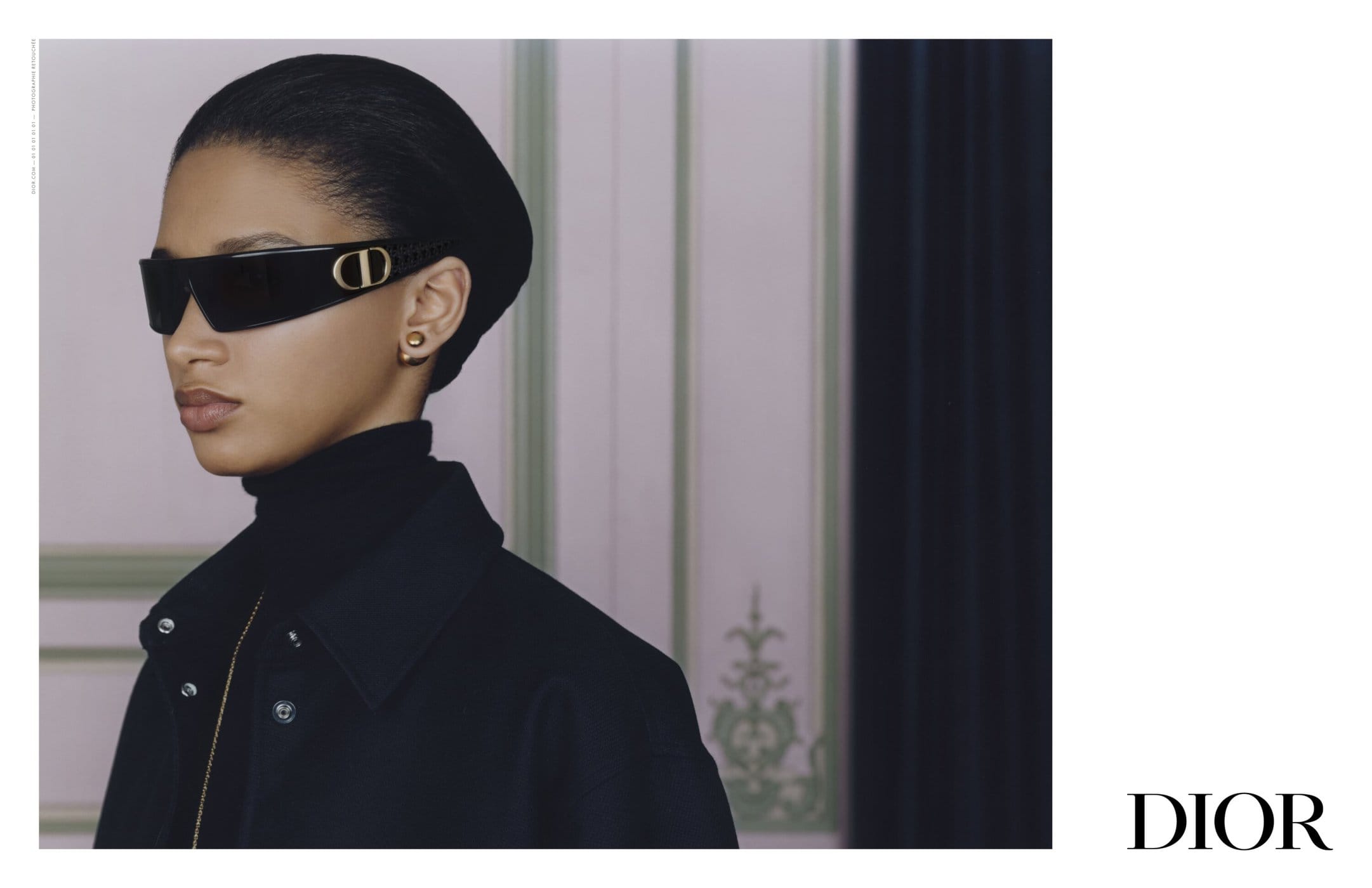 Model wearing dark wrap sunglasses and a black jacket against a classical interior backdrop for Dior.