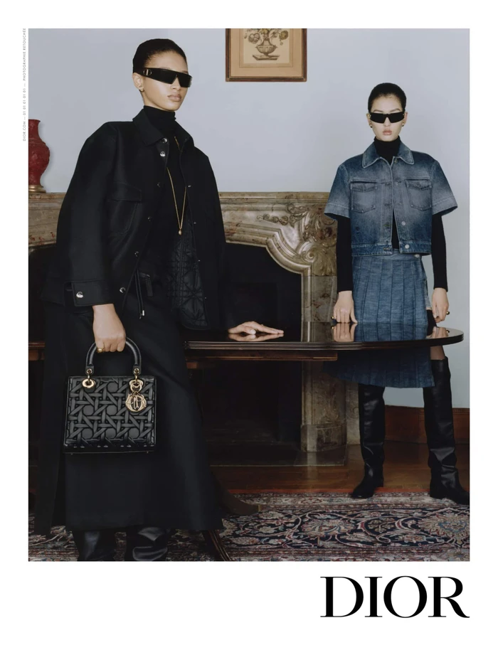 Two models wearing dark sunglasses and black turtlenecks standing near a fireplace for Dior Fall 2024 campaign