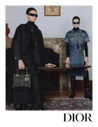 Two models wearing dark sunglasses and black turtlenecks standing near a fireplace for Dior Fall 2024 campaign