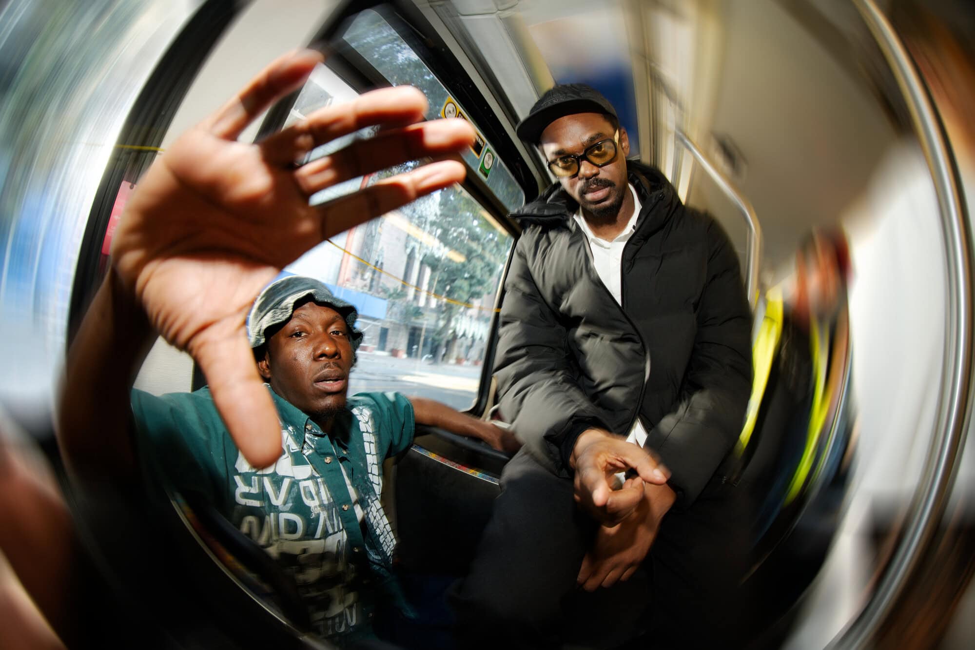 Two adult men are sitting inside a public transport vehicle with a wide angle lens creating a fisheye effect, emphasizing perspective and space.