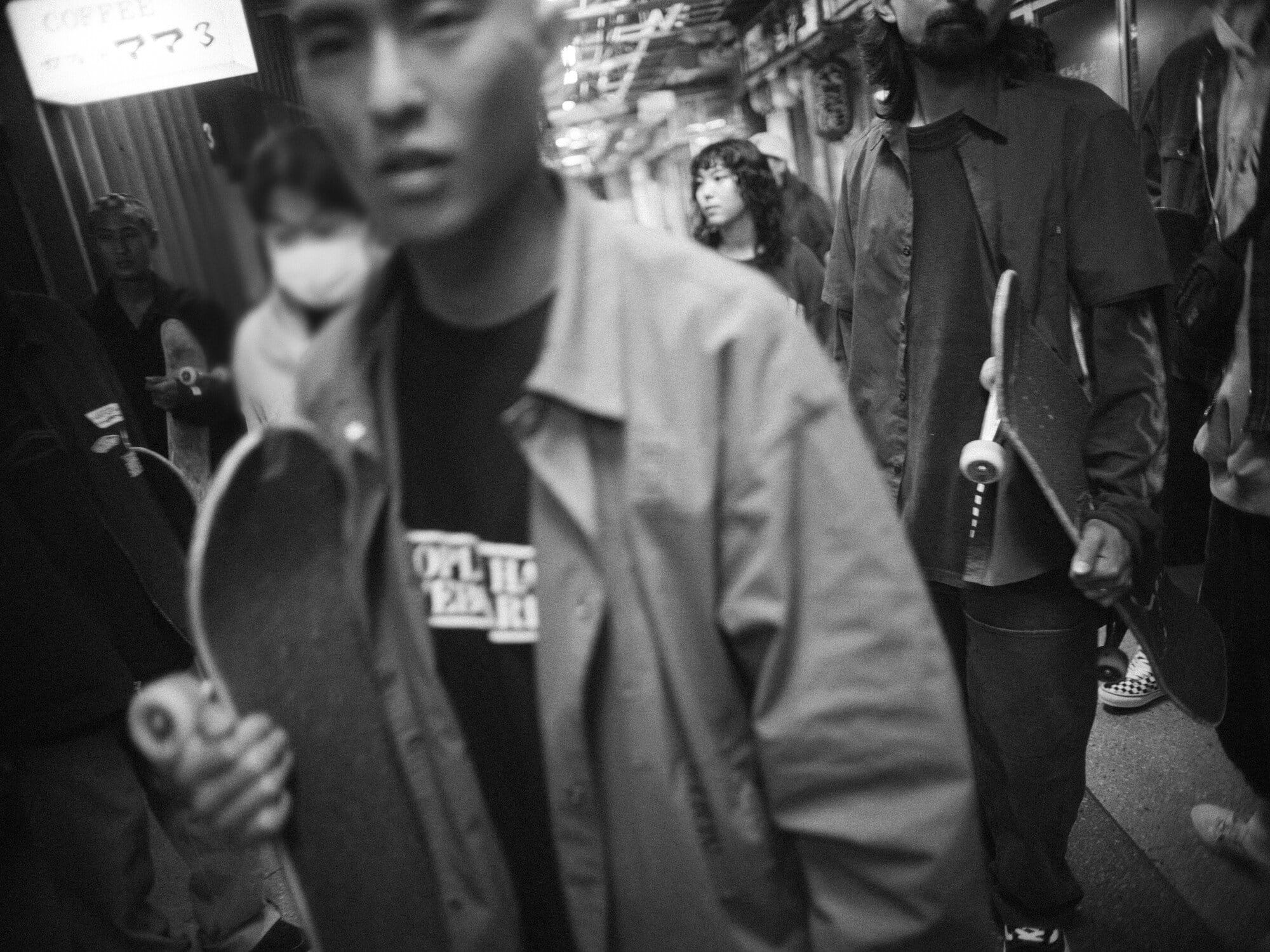 Black and white shot of a group of people with skateboards standing in an urban environment with an indoor setting.