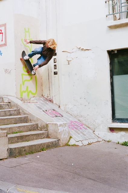 Male skateboarder in mid-air performing a trick on a skateboard, going off the side of a building with graffiti, and steps nearby.
