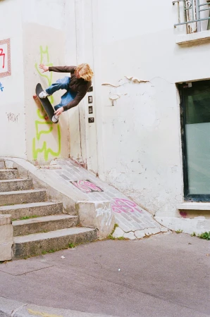 Male skateboarder in mid-air performing a trick on a skateboard, going off the side of a building with graffiti, and steps nearby.
