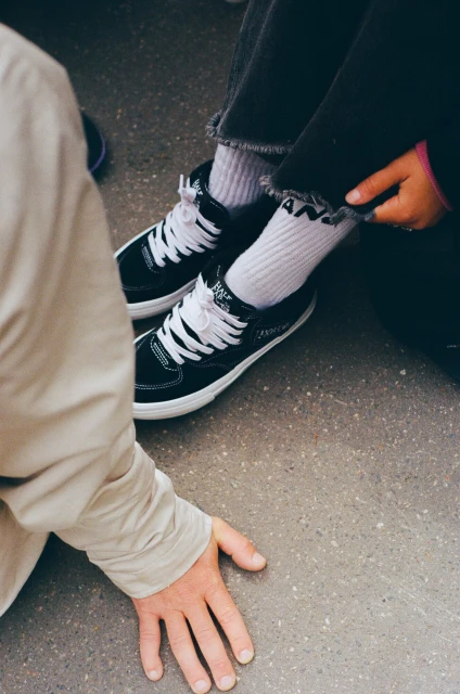 Eye-level shot capturing the trendy style of black and white Vans sneakers paired with white socks and dark jeans on a gray concrete surface.