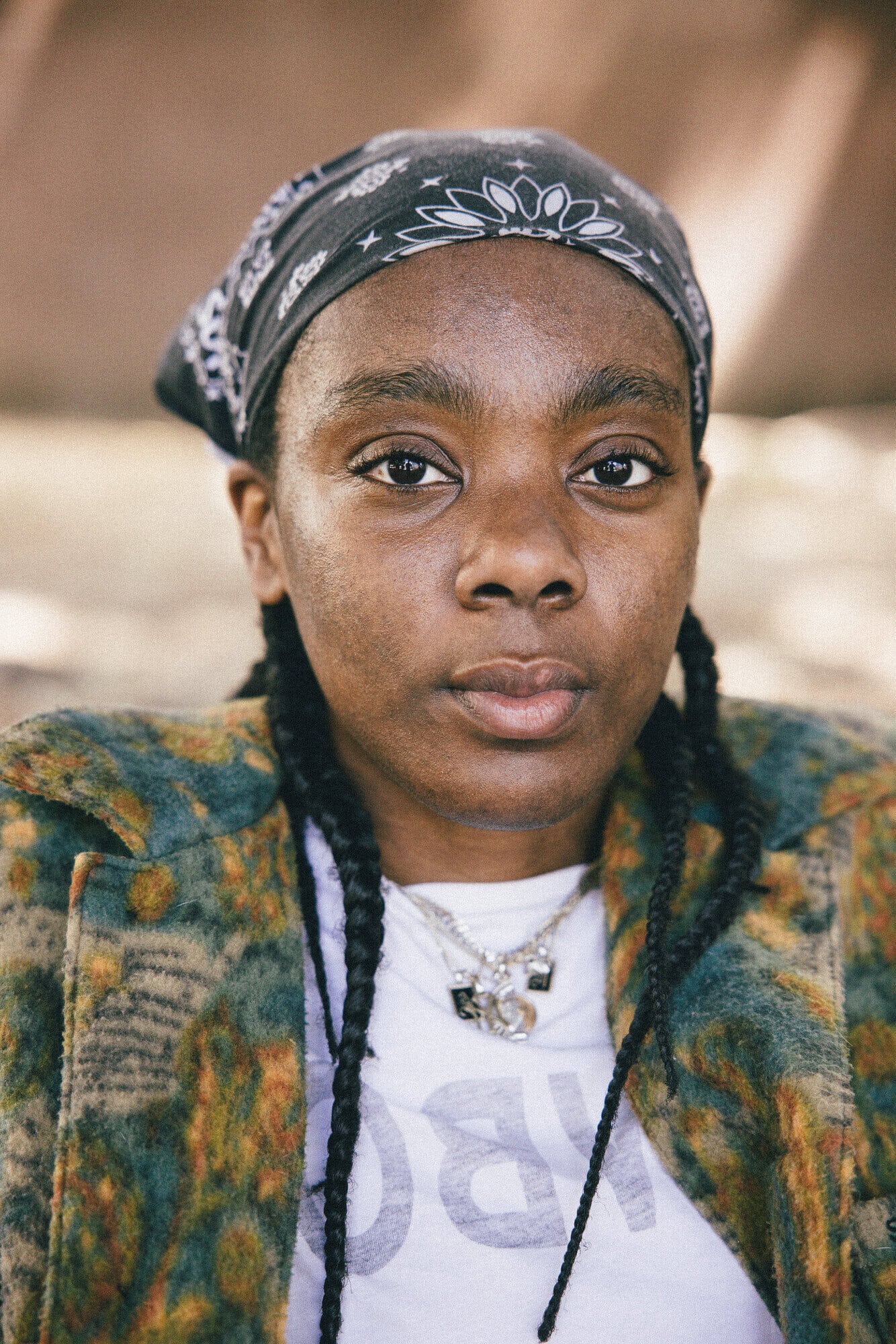 Close-up portrait of an African American woman with a headscarf, silver necklaces, and a patterned jacket looking directly at the camera.