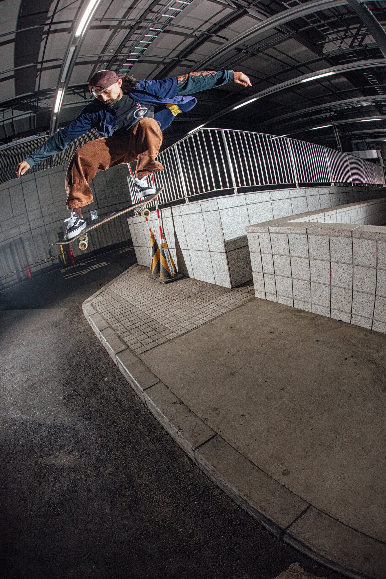 Young adult male performing a skateboard trick in an urban environment with an eye-level angle and grey color palette.