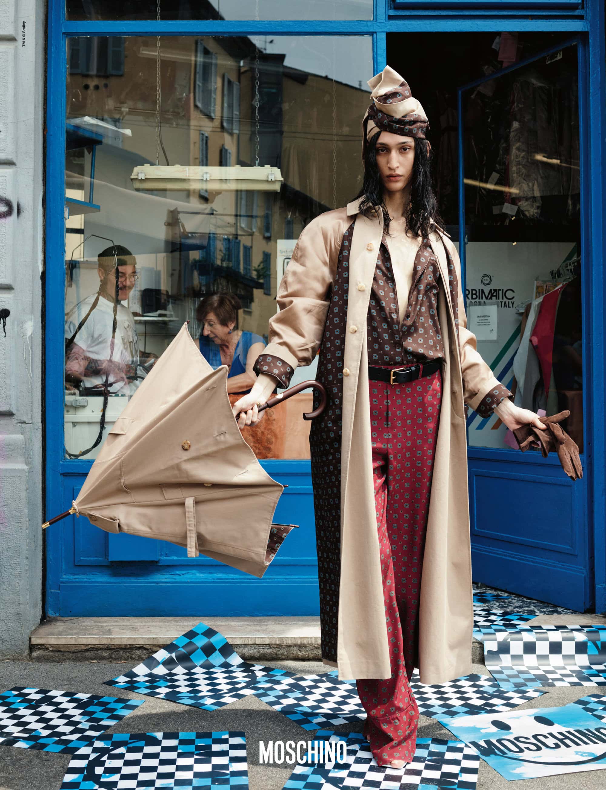 Fashionable woman in patterned outfit standing in front of a blue building holding an umbrella, outdoor fashion editorial shot.