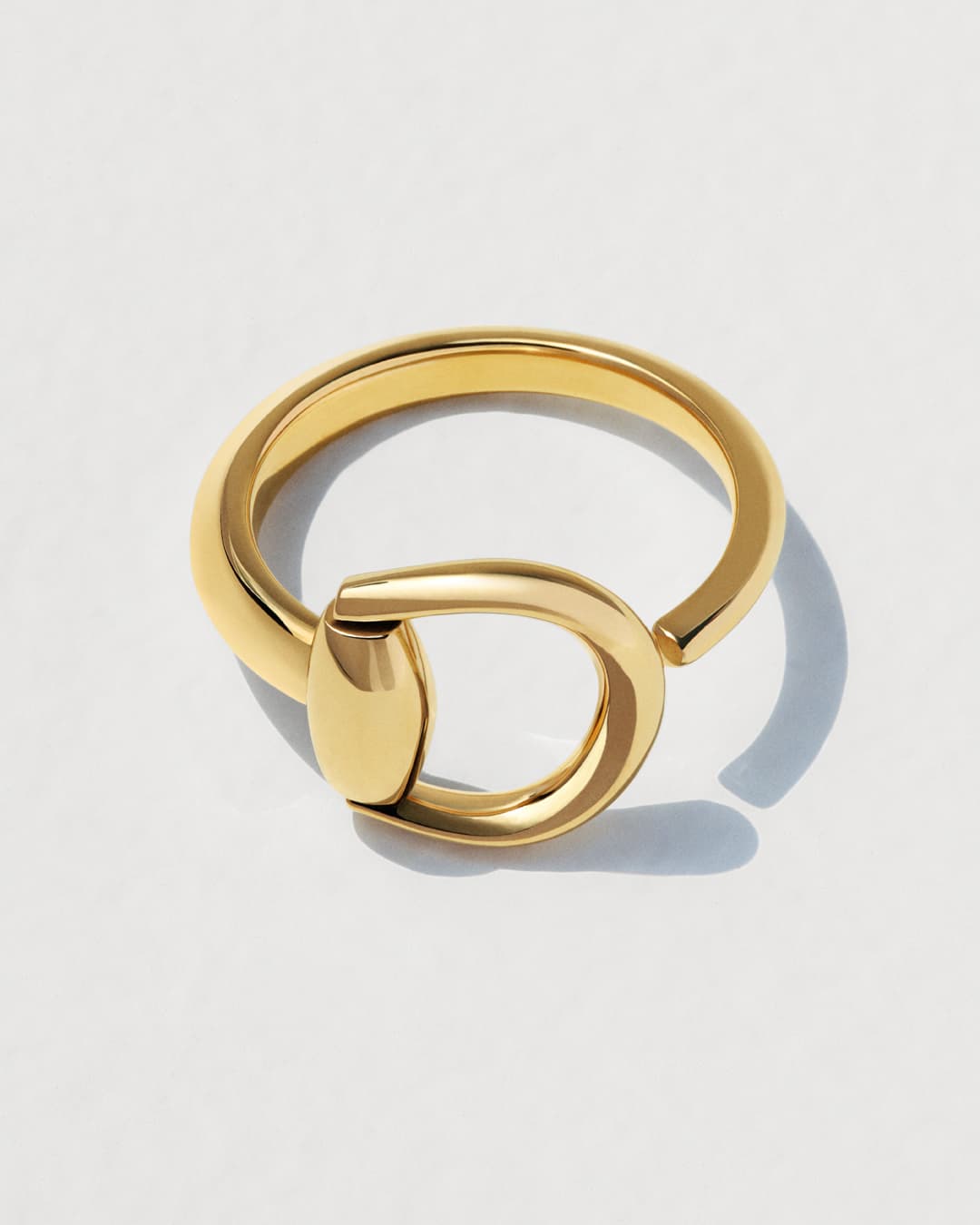 Close-up of a modern gold metal ring with a unique design, set against a clean white background, capturing a sense of minimalistic luxury.
