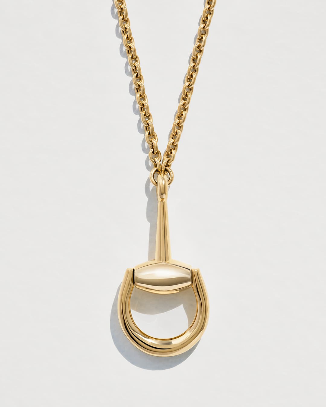 Gold necklace with horsebit pendant on a white background. Chain and pendant jewelry fashion, equestrian style.