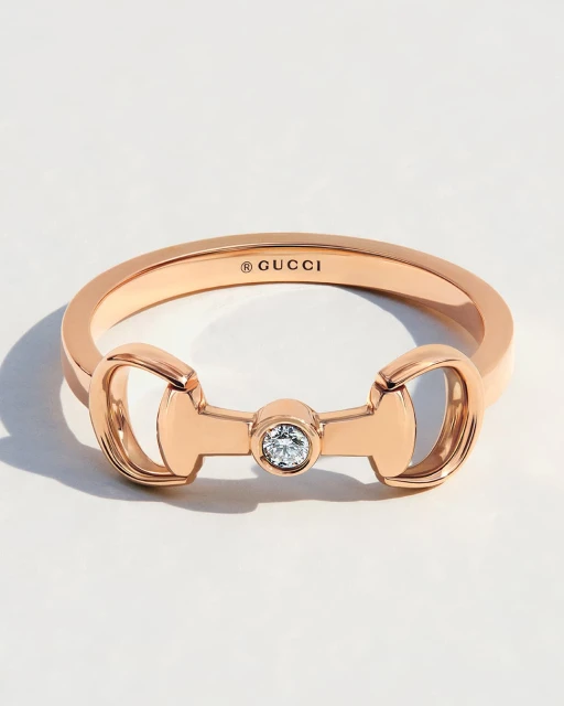 Close-up shot of a gold-colored ring with a circular crystal on a white surface, showcasing luxury jewelry and minimalist design.