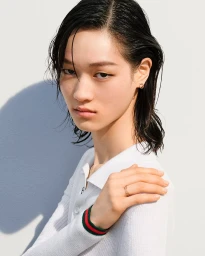 Model with slicked-back dark wet hair wearing a white polo shirt with striped collar trim against a white background