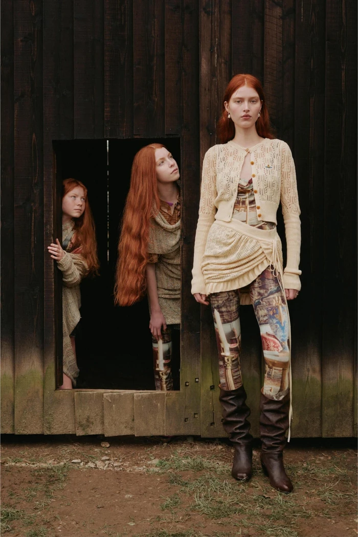 Three red-haired models posing outdoors in front of a dark wooden building for Vivienne Westwood Pre-Fall 2024 campaign.