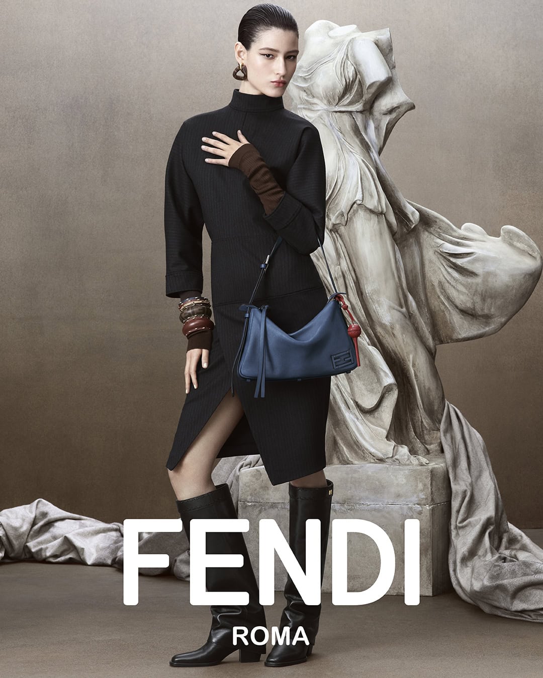 Fashion shot of a woman in a black dress with a blue purse standing next to a white sculpture with the brand name FENDI ROMA.