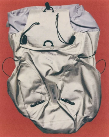 Open grey nylon backpack showcasing its inner compartments and drawstrings, set against a red background in a studio setting.