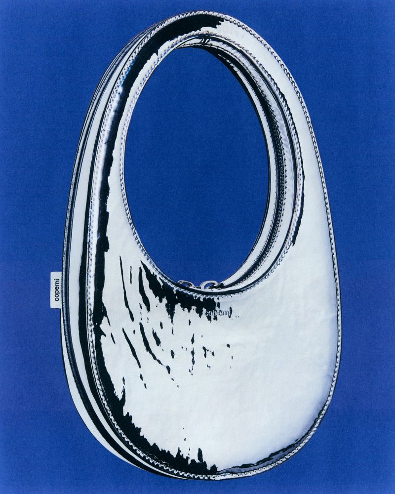 Shiny silver Coperni Swipe handbag on a blue background. Fashion accessory with a glossy surface. Minimalist studio product shot.