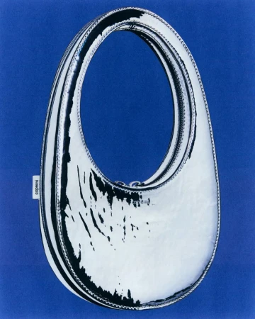 Shiny silver Coperni Swipe handbag on a blue background. Fashion accessory with a glossy surface. Minimalist studio product shot.