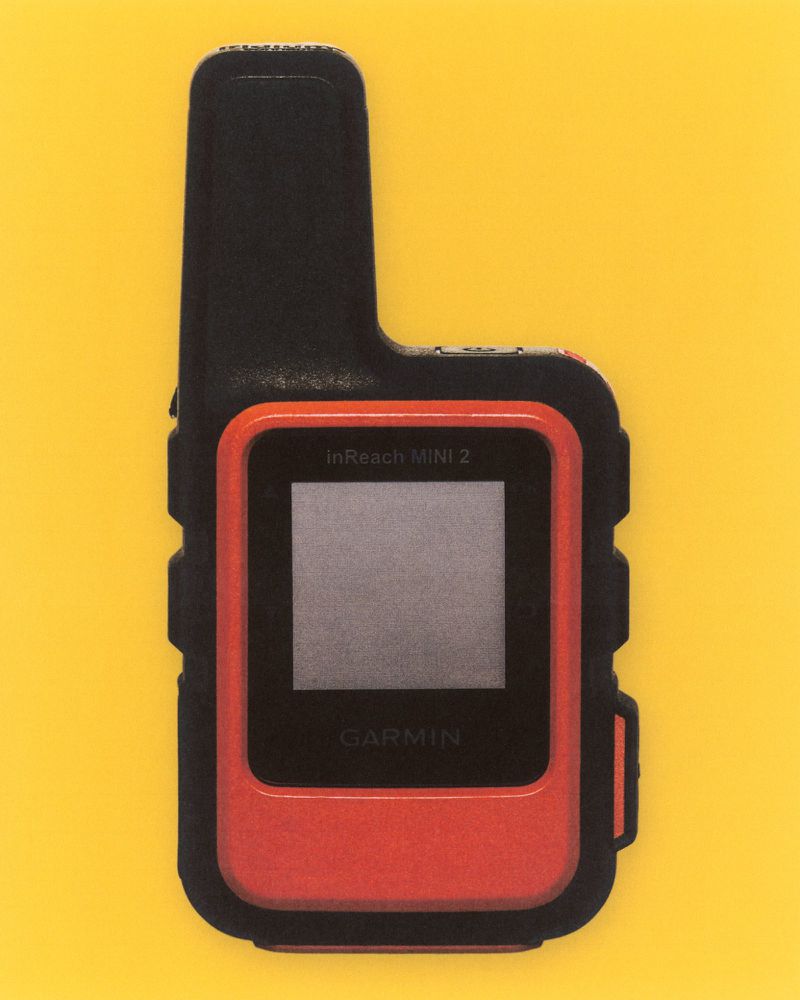 Garmin inReach Mini 2 satellite communicator. A handheld device with a black and orange casing on a yellow background. 