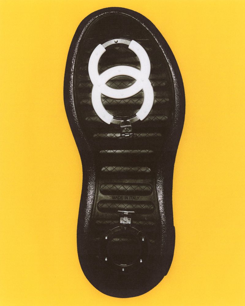 Close-up studio shot of the sole of a black fashion shoe, showcasing a white interlocking circle design on a bright yellow background.