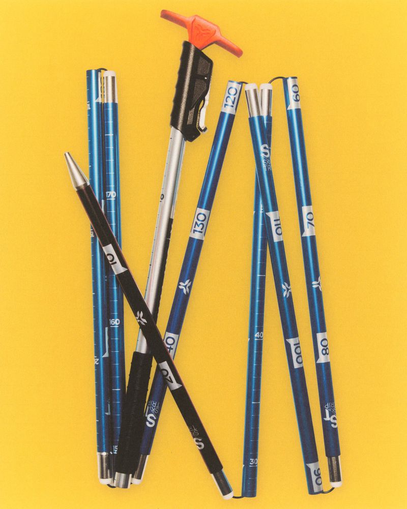 Several blue, silver and black trekking poles are arranged on a yellow background, showcasing their adjustable lengths and handles.