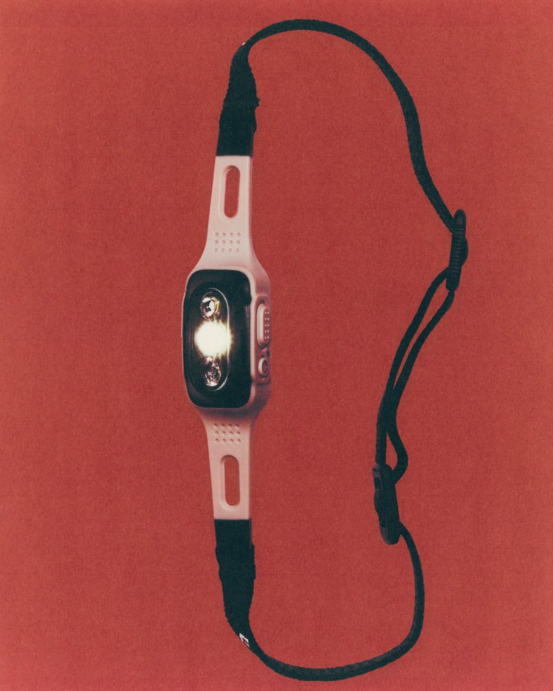 Close-up of a modern LED headlamp with a white band and black strap against a plain red background, showcasing its design and function.