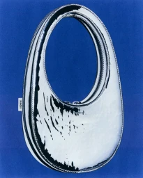 Silver metallic oval handbag with distressed black markings on a bold solid blue background.