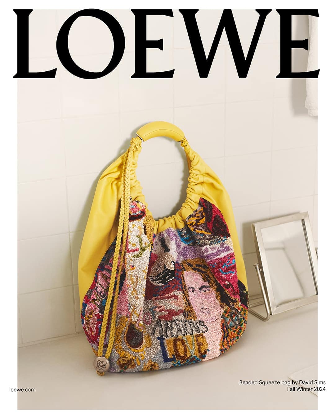Loewe Beaded Squeeze bag featuring artwork on a bathroom sink against a tiled white wall, showcasing fashion and brand aesthetic.