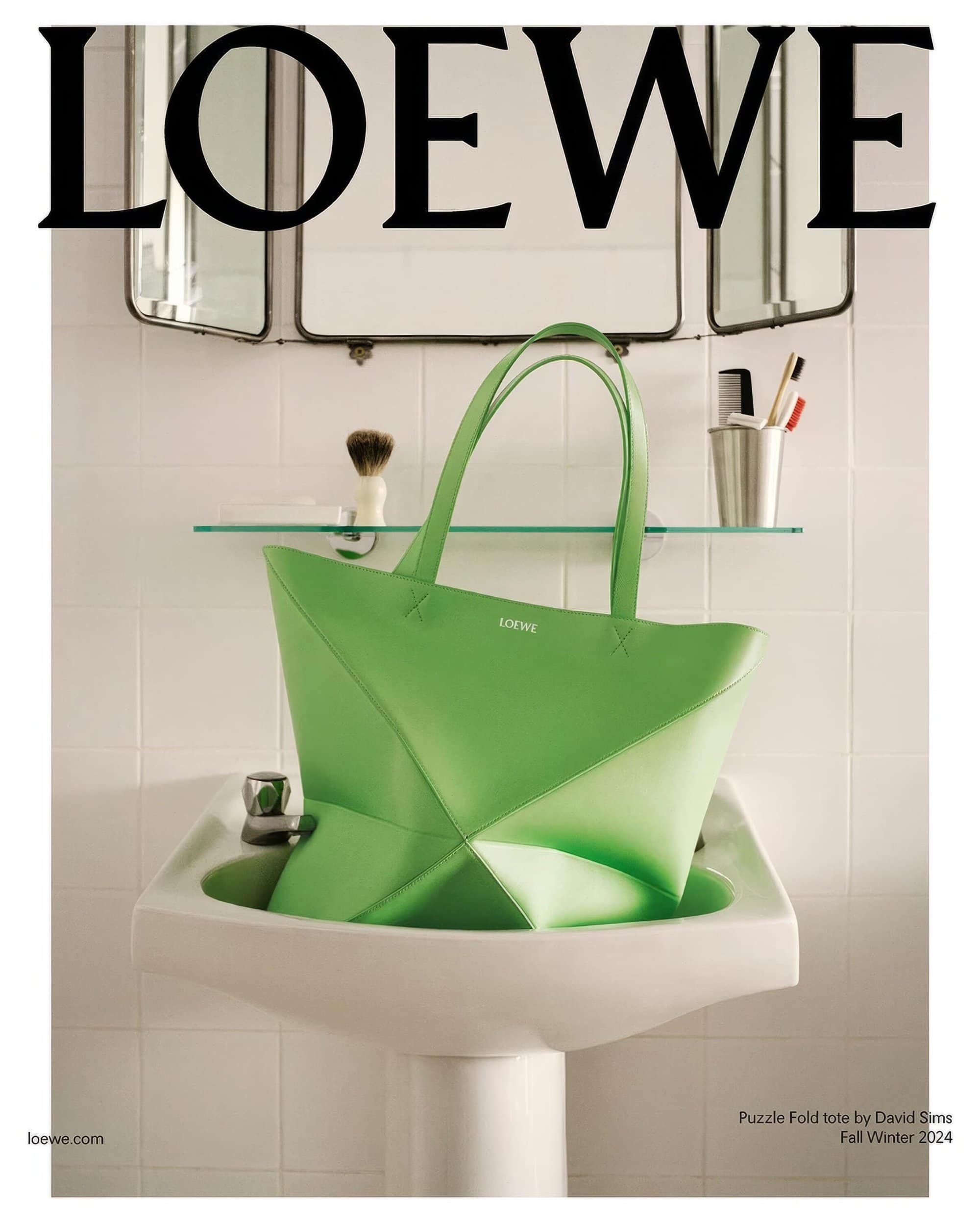 Loewe Puzzle Fold tote bag in bright green, displayed in a bathroom sink next to a chrome faucet and against a white tiled wall.