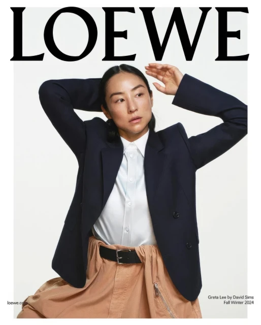 Fashion editorial shot of an Asian adult female model in a navy blazer, white top, and tan skirt, against a white backdrop with Loewe logo.