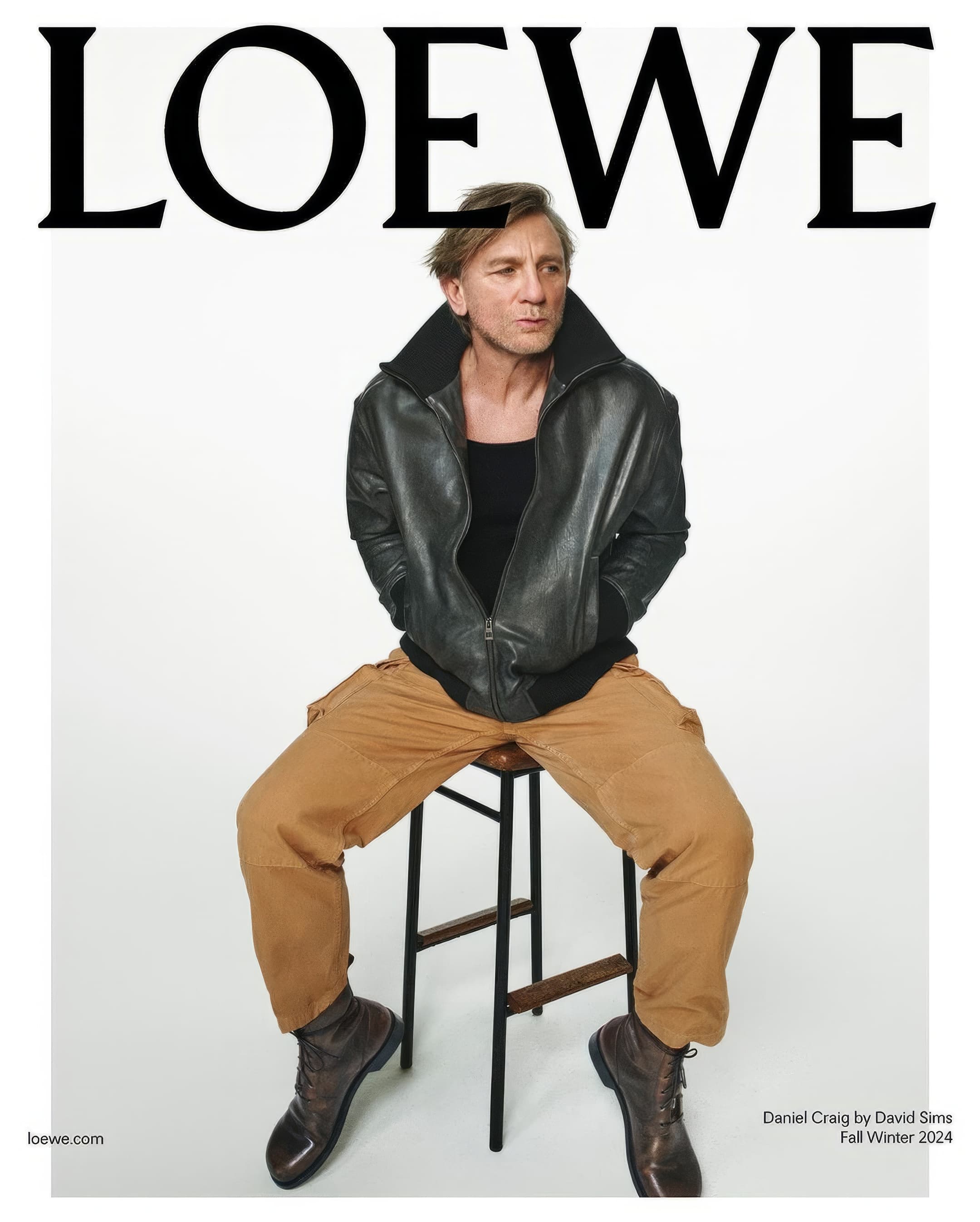 Daniel Craig sits on a stool wearing a leather jacket and cargo pants. He is posing for a Loewe Fall/Winter 2024 magazine cover.