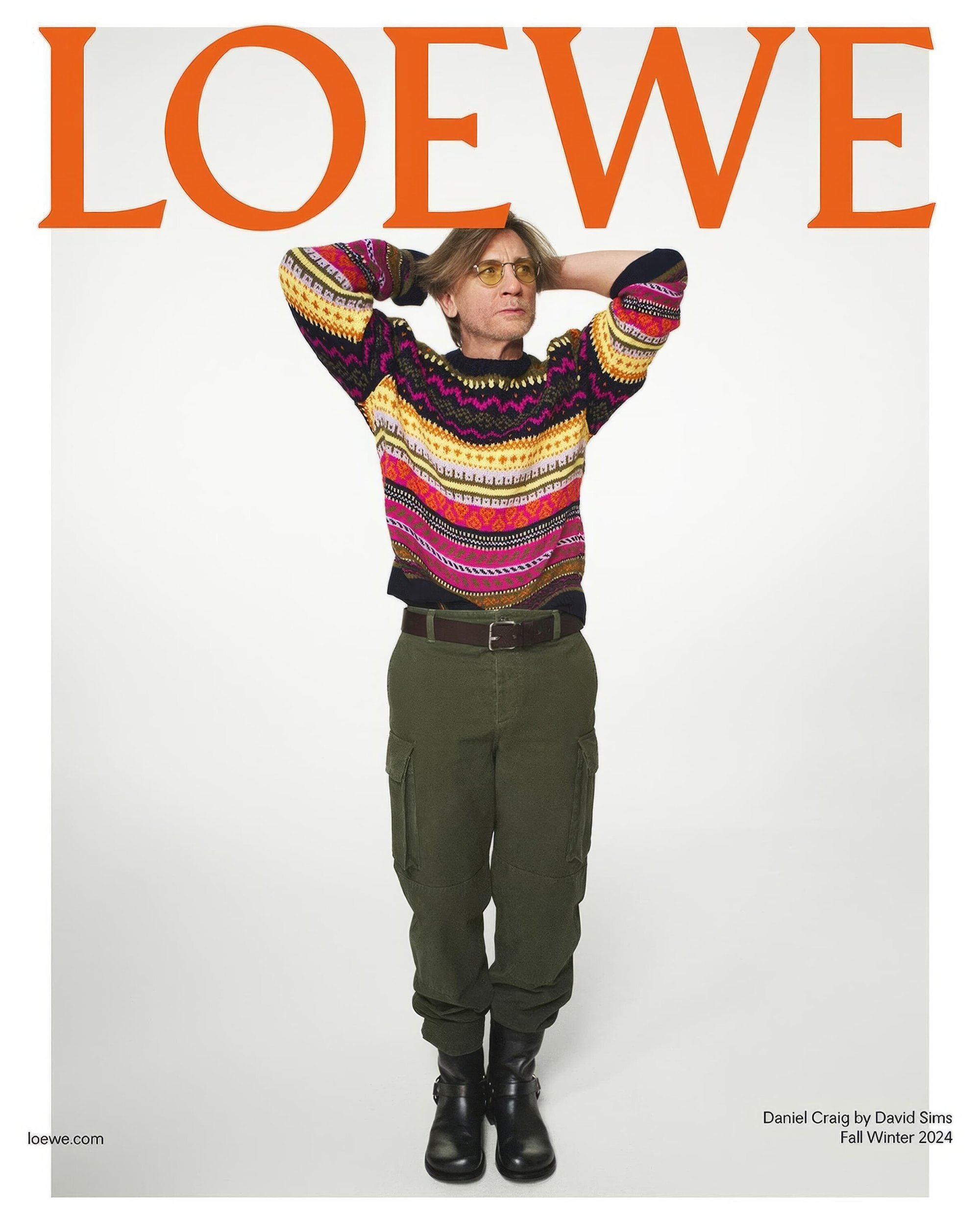 A full-length portrait of Daniel Craig wearing a colorful sweater and cargo pants for a Loewe Fall/Winter 2024 fashion advertisement.