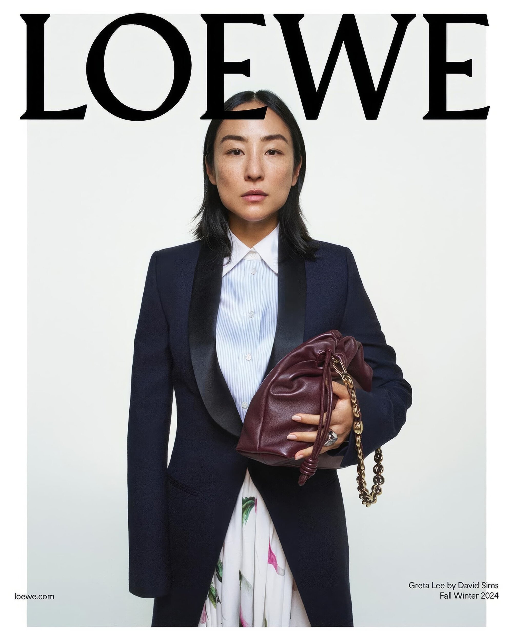 Elegant portrait of an Asian woman holding a burgundy purse. She is wearing a navy tuxedo jacket over a white shirt and floral skirt.