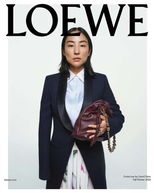 Elegant portrait of an Asian woman holding a burgundy purse. She is wearing a navy tuxedo jacket over a white shirt and floral skirt.