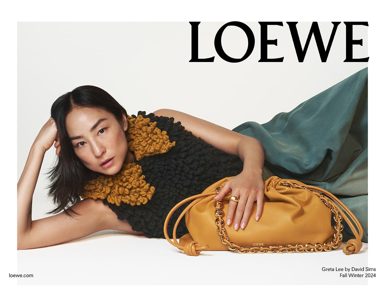 Asian woman poses with a Loewe bag, featuring a drawstring closure and chain strap, against a neutral backdrop for a fashion editorial.
