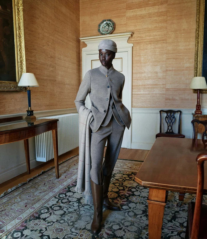 Model wearing a matching knit jacket and trousers with a beanie hat and boots standing in an interior room.