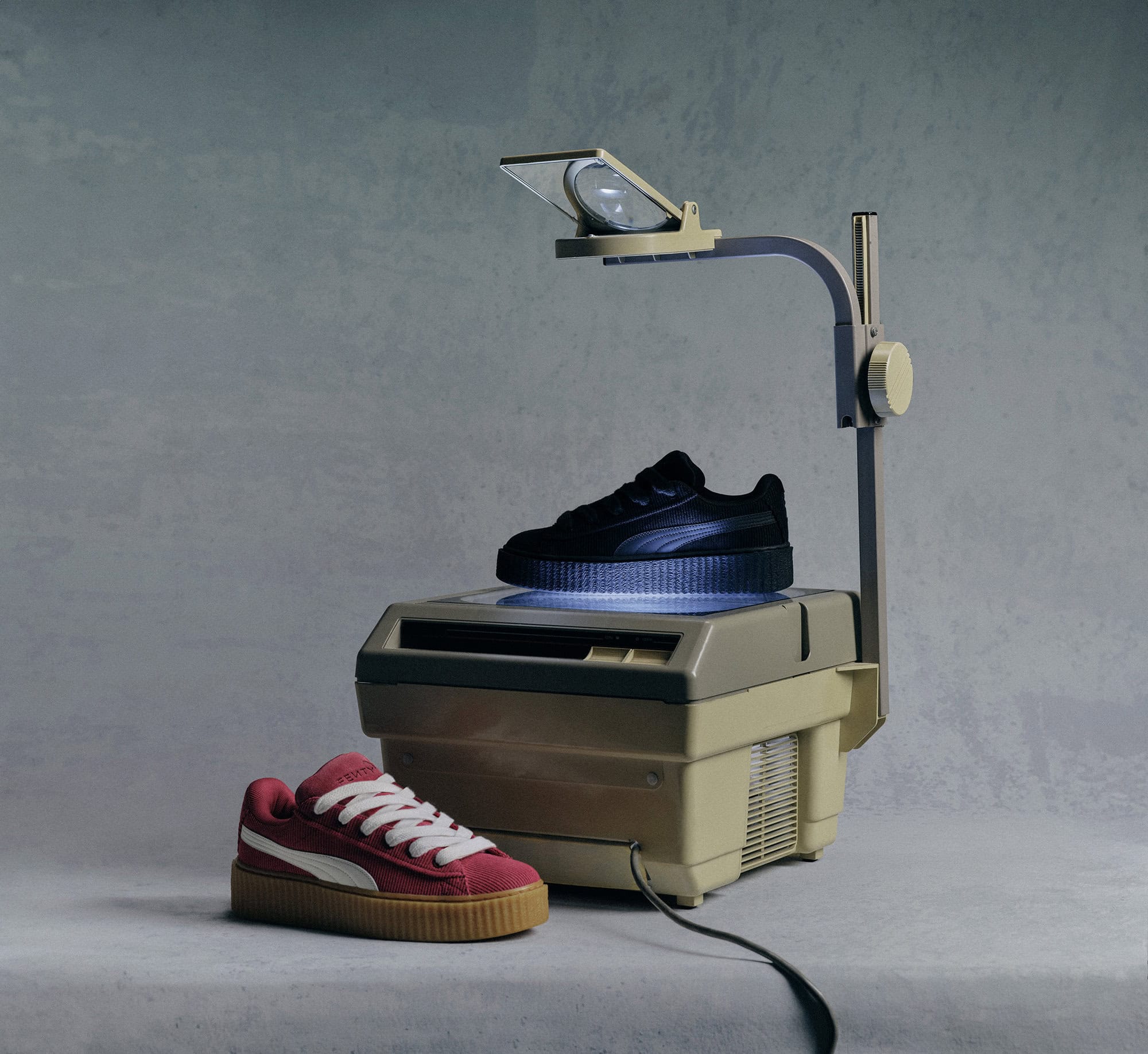 Two Puma sneakers displayed on a vintage overhead projector in a studio setting, featuring one black and one pink sneaker.