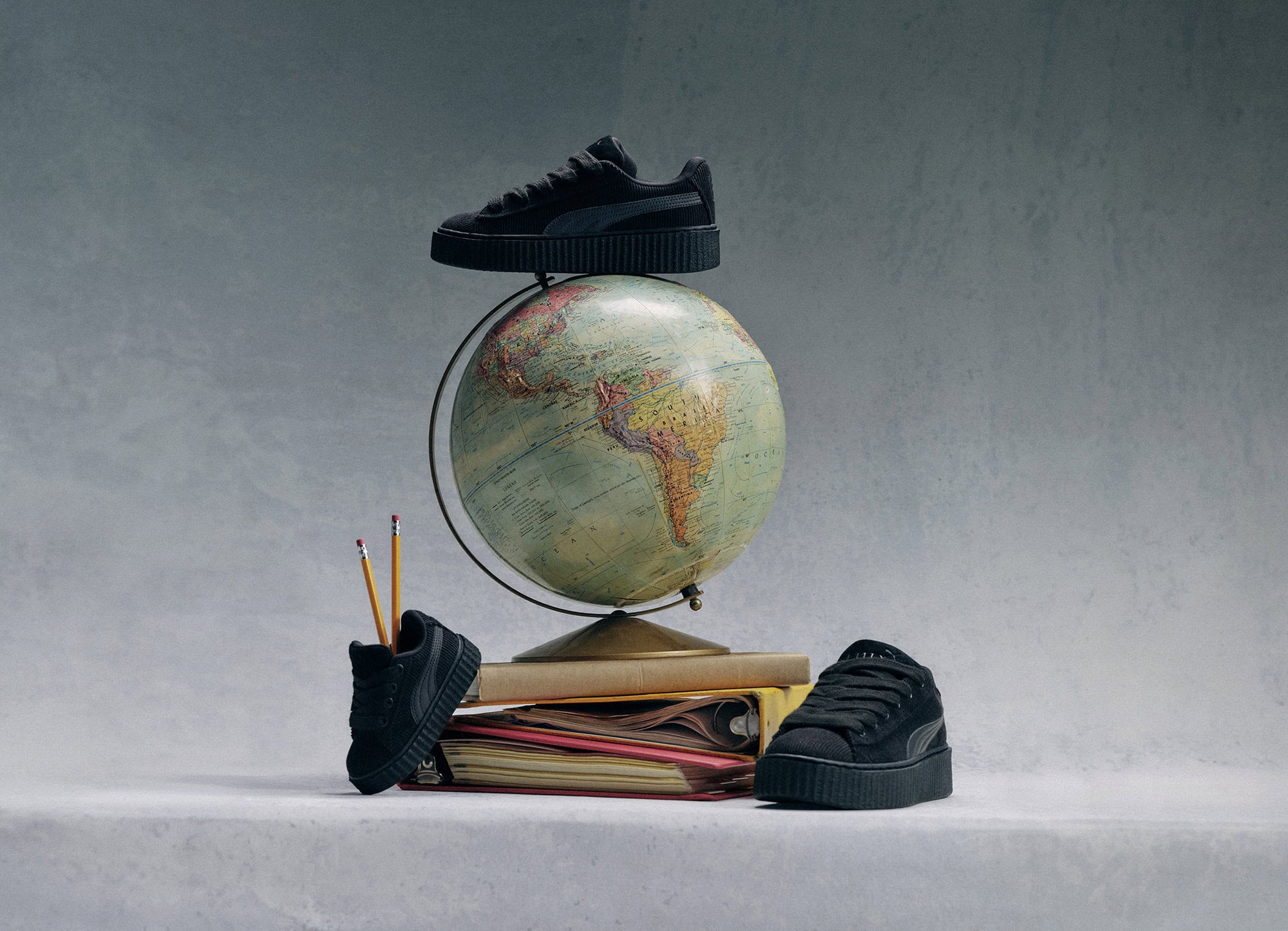 A product still life shot featuring a stack of books with an antique globe. Three black shoes are balanced around the globe.