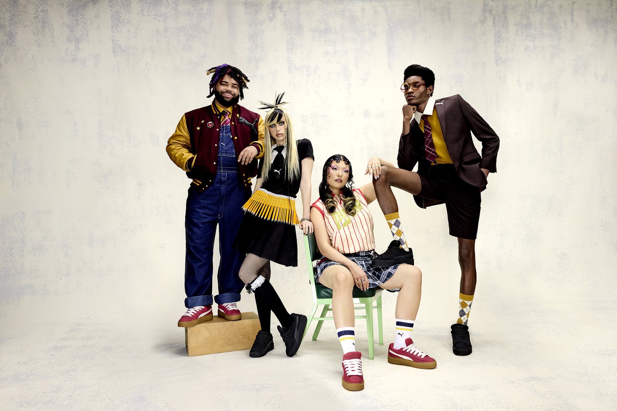 Group of four diverse fashion models in retro school-inspired outfits and sneakers posing in a bright studio setting.