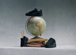Black platform sneakers arranged around a vintage world globe resting on stacked books against a neutral grey studio backdrop.