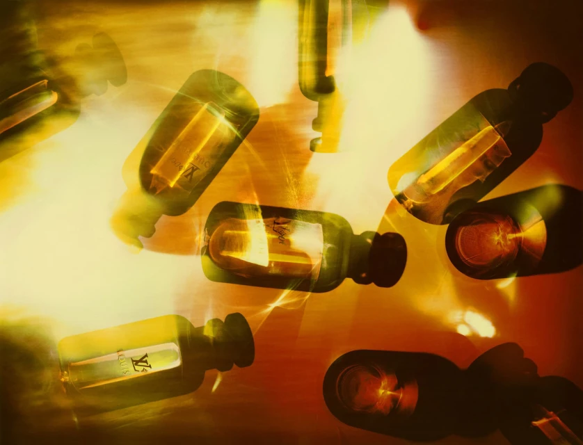 Multiple transparent glass bottles with gold liquid inside, arranged on a surface with blended yellow, gold, and red lighting.