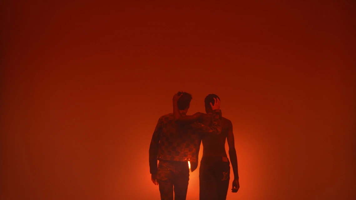 Two people pose in a studio with orange lighting, wearing jackets and pants in a medium shot, creating a dramatic and fashionable silhouette.